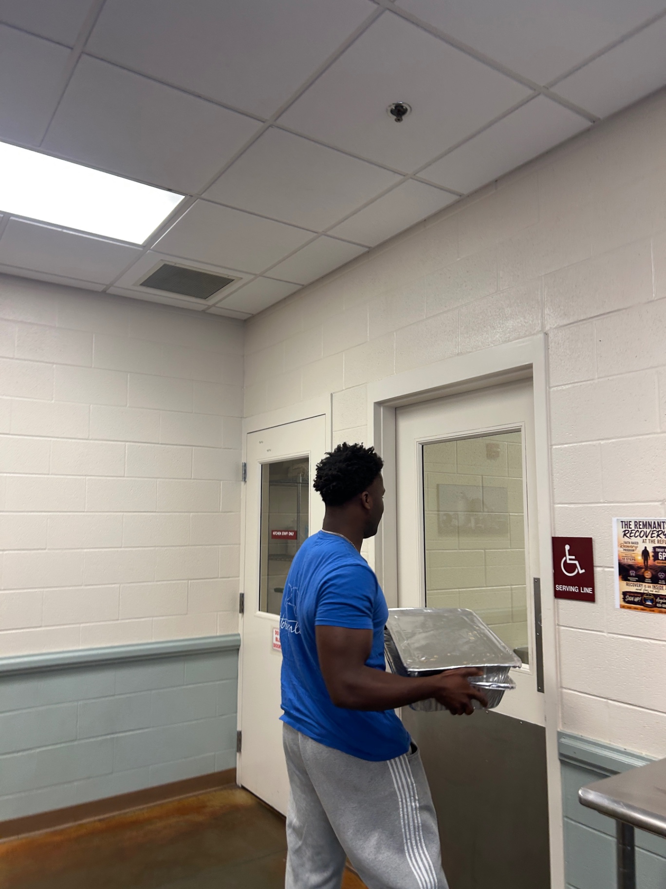 Daniel carrying covered food trays toward the serving line doors at The Salvation Army
