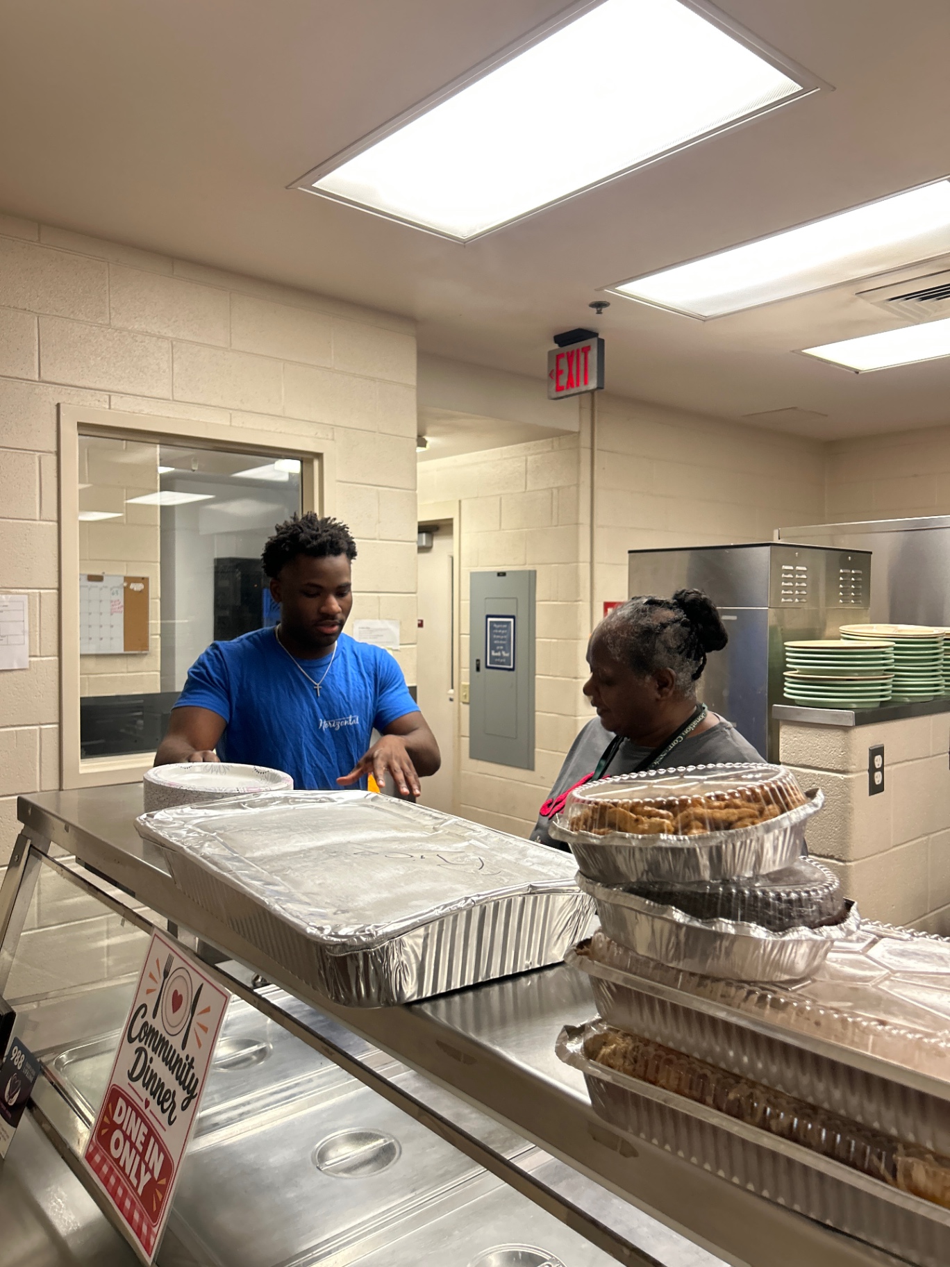 Daniel and a woman beside trays of food at a serving counter