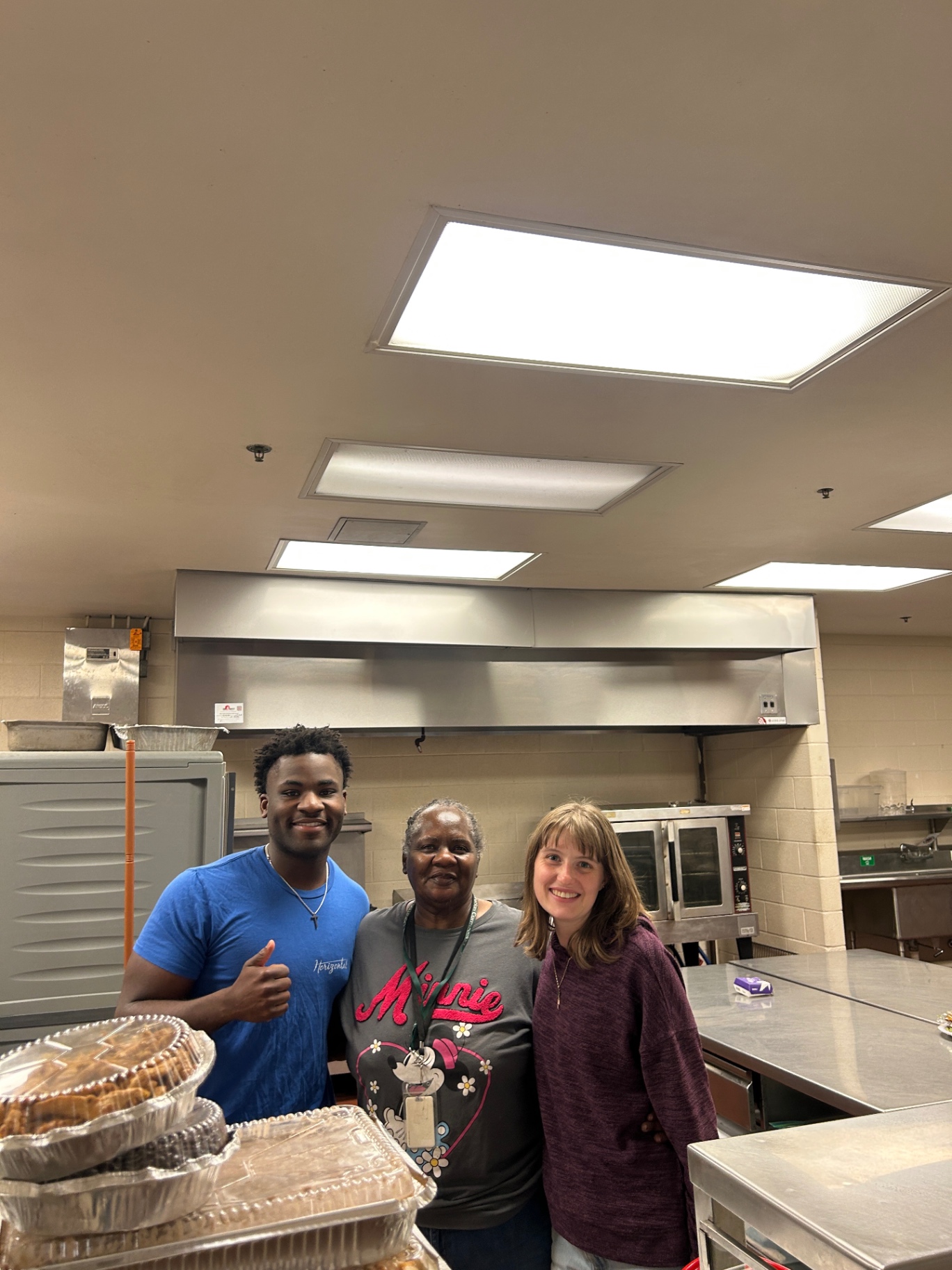 Daniel giving a thumbs up with two kitchen team members beside covered dishes