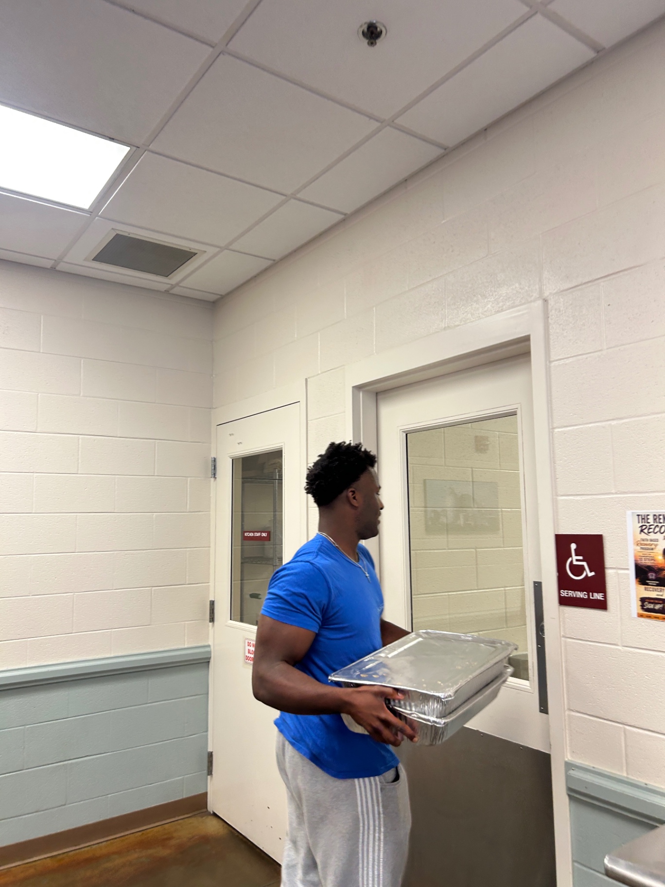 Daniel carrying covered food trays through a serving area