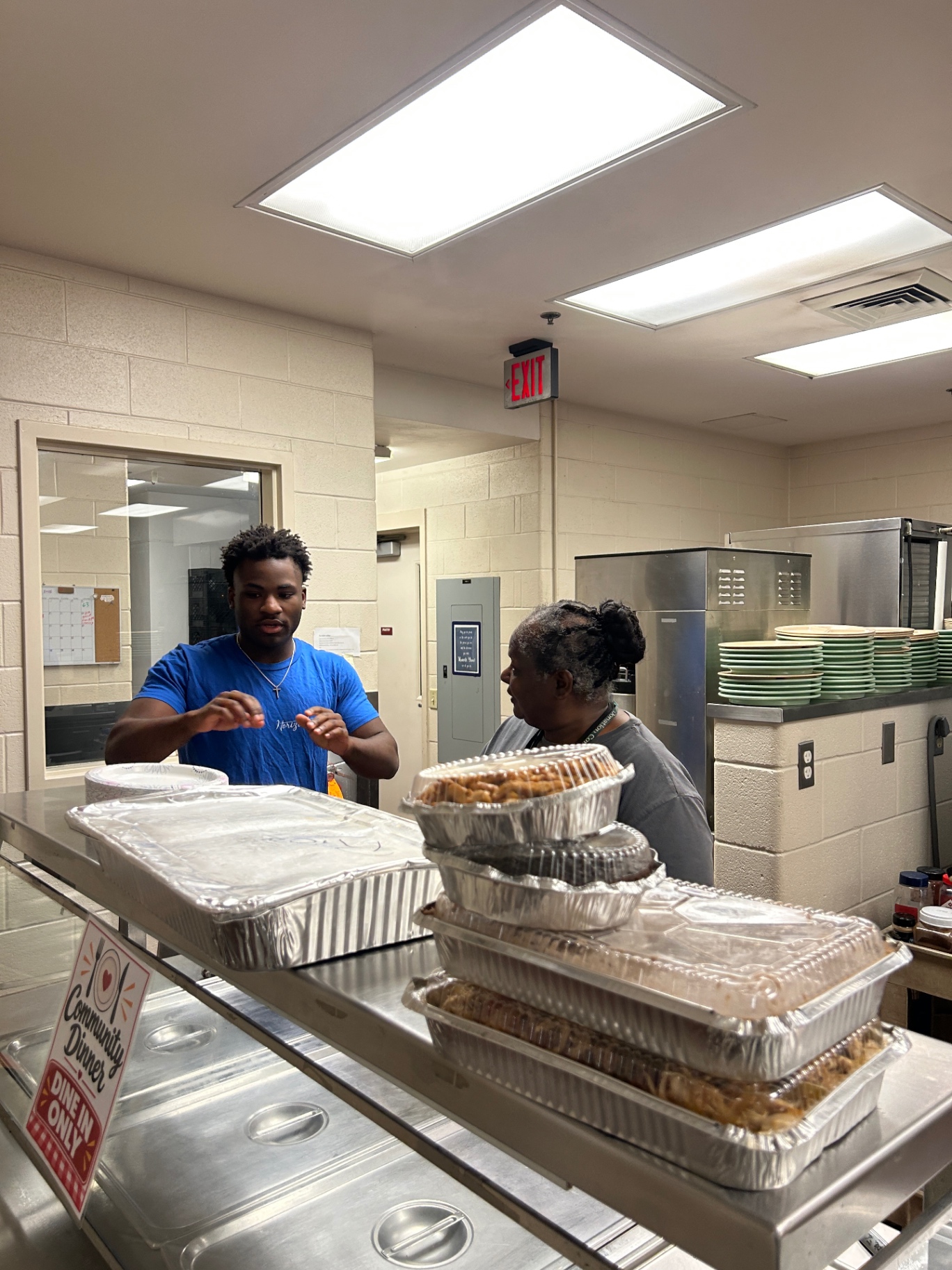 Daniel talking with a kitchen team member beside trays of food at the serving counter